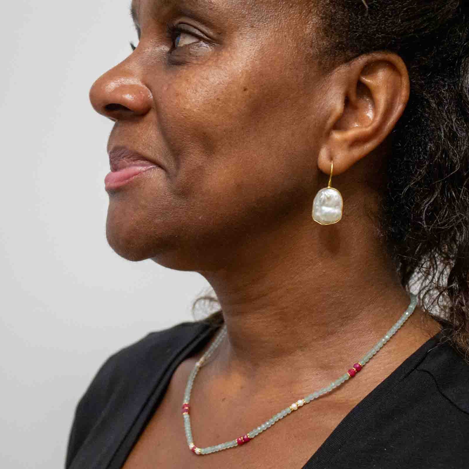Woman wearing a pearl earring and necklace against a plain background