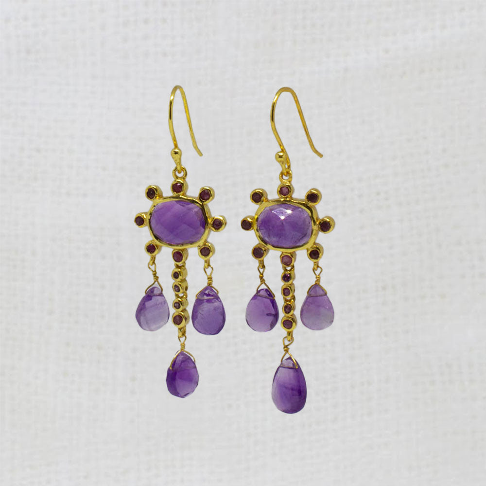 Pair of gold earrings with purple amethyst and red ruby gemstones on a white background