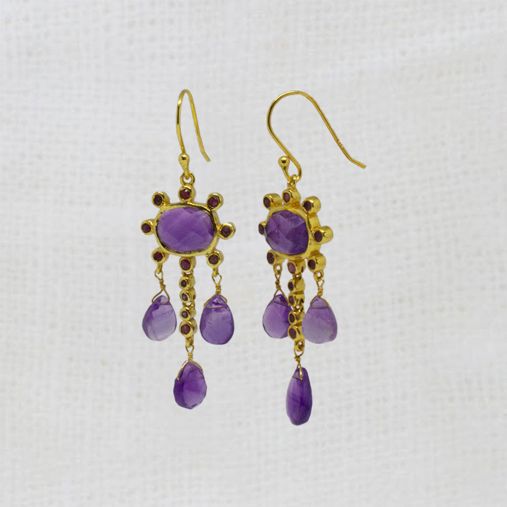 Pair of gold earrings with purple amethyst and red ruby gemstones on a white background