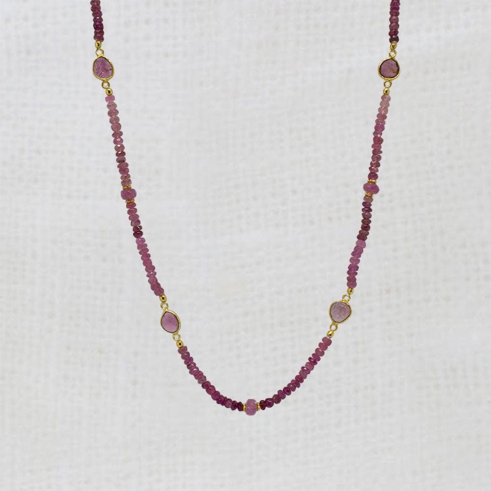 Necklace with pink sapphire gemstone beads and gold accents on a white background