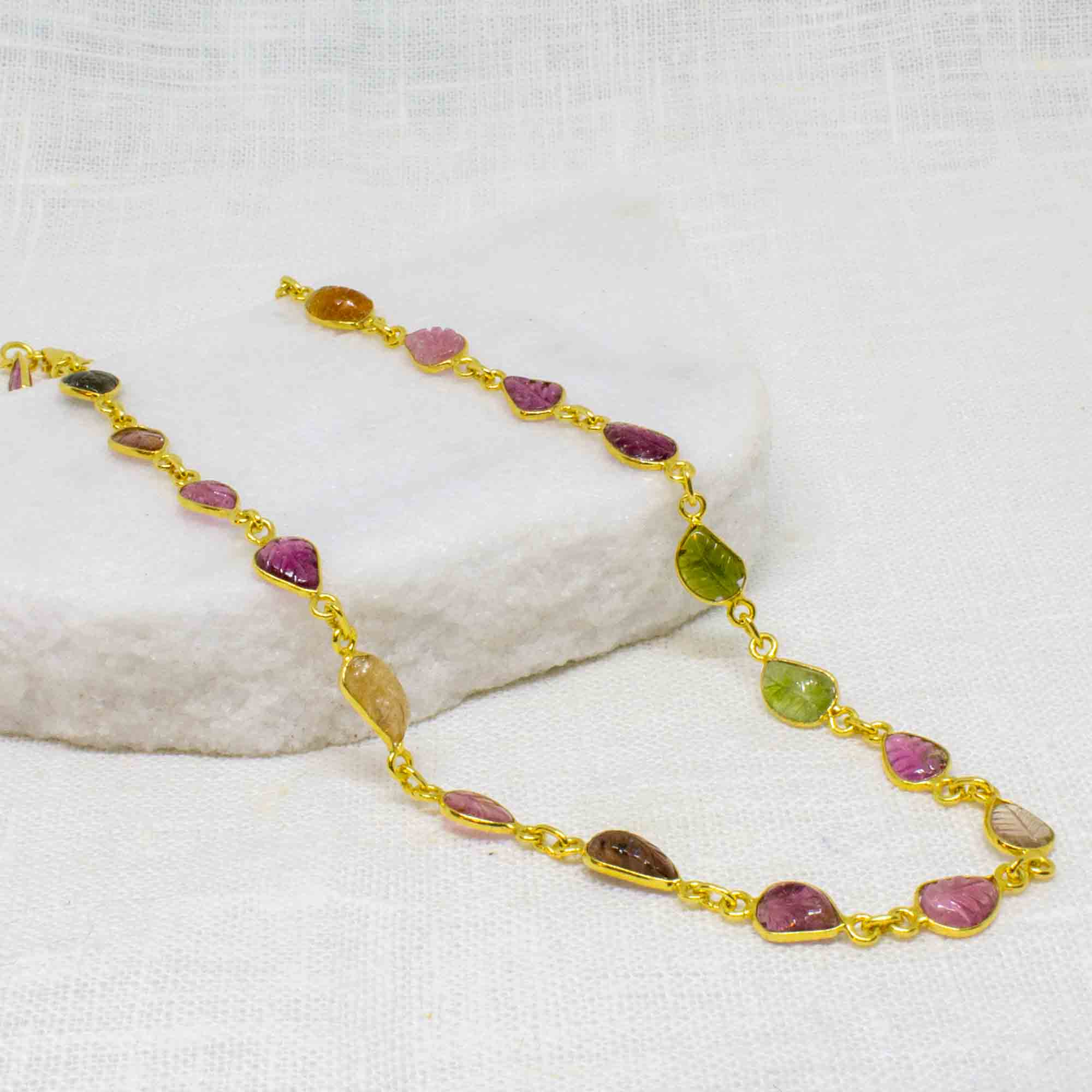 A short gold vermeil necklace with carved tourmaline gemstones, displayed on a white surface.