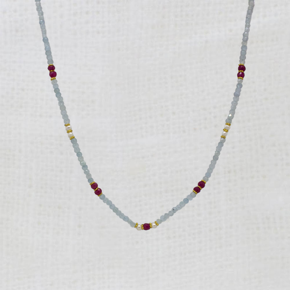 Necklace with small aquamarine, pearl and ruby beads on a white fabric background