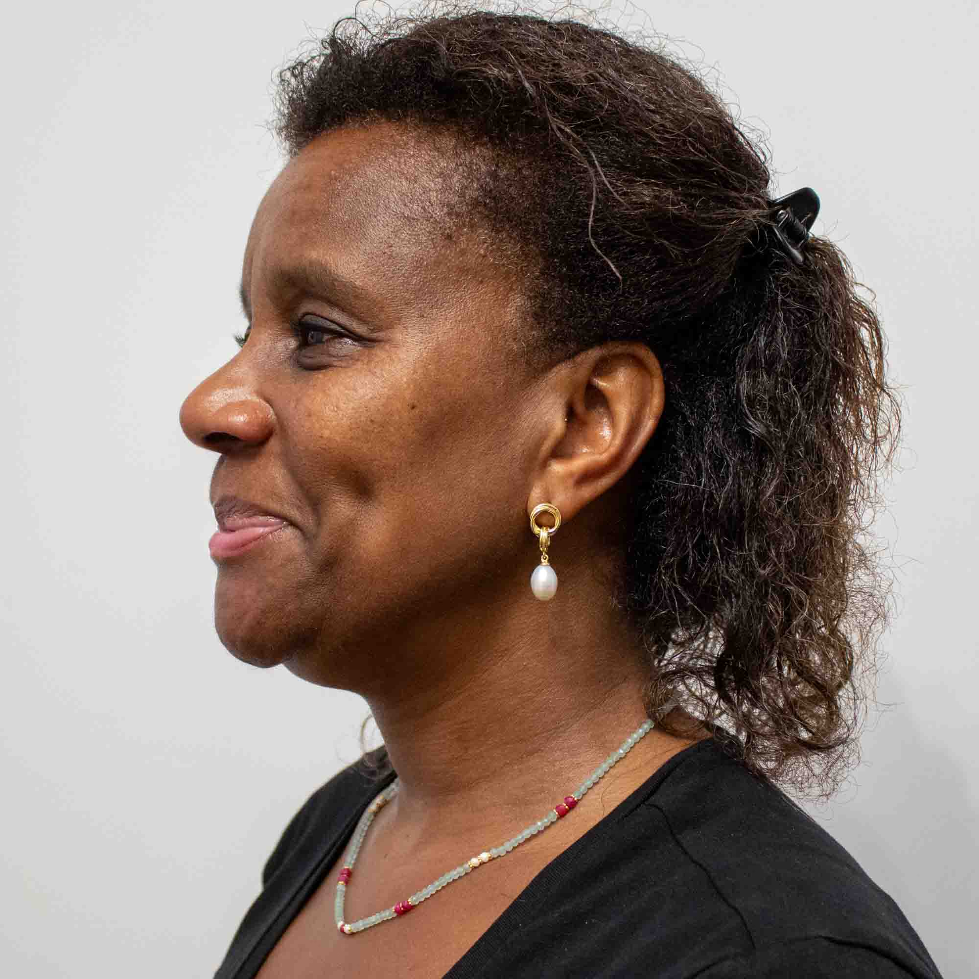 Woman with gemstone beaded necklace and pearl earrings on a plain background