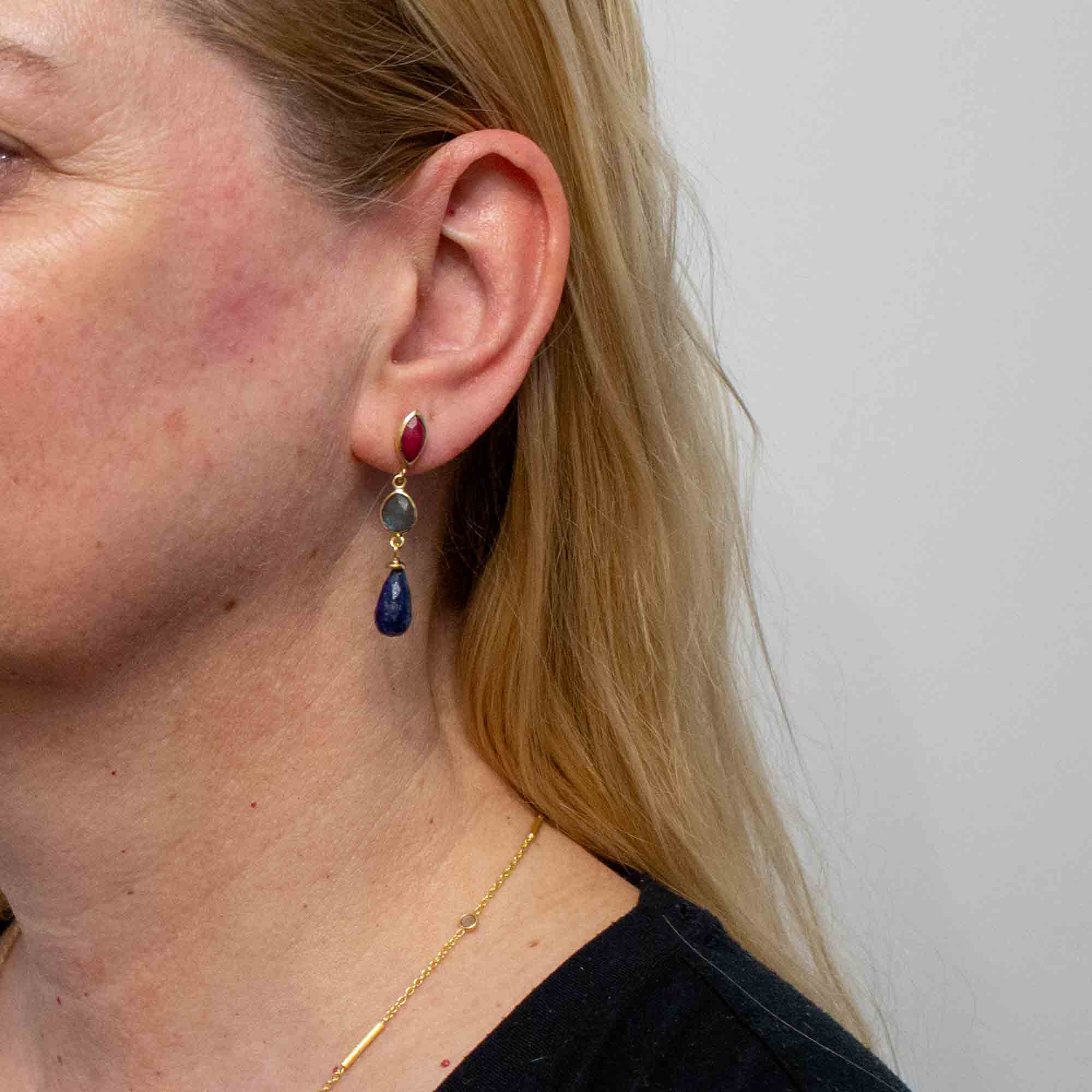 Model wearing gold earrings with ruby, labradorite and lapis gemstones