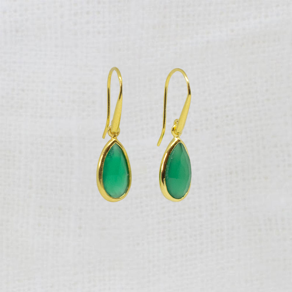 A pair of gold drop earrings with teardrop-shaped green onyx gemstones, displayed on a textured white fabric background.