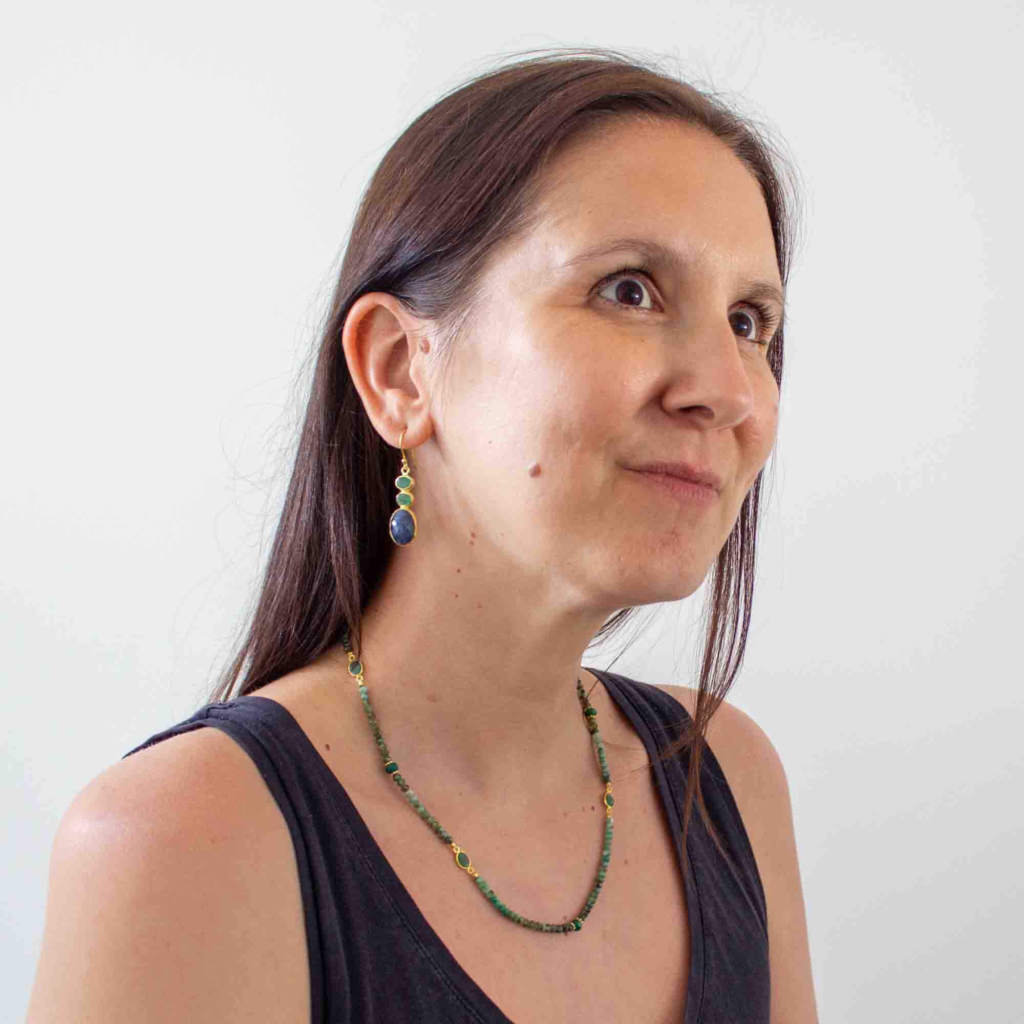 Model wearing a pair of blue sapphire and emerald earrings and green emerald beaded necklace. 