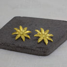 Large brushed gold vermeil daisy flower stud earrings displayed on a dark grey slate