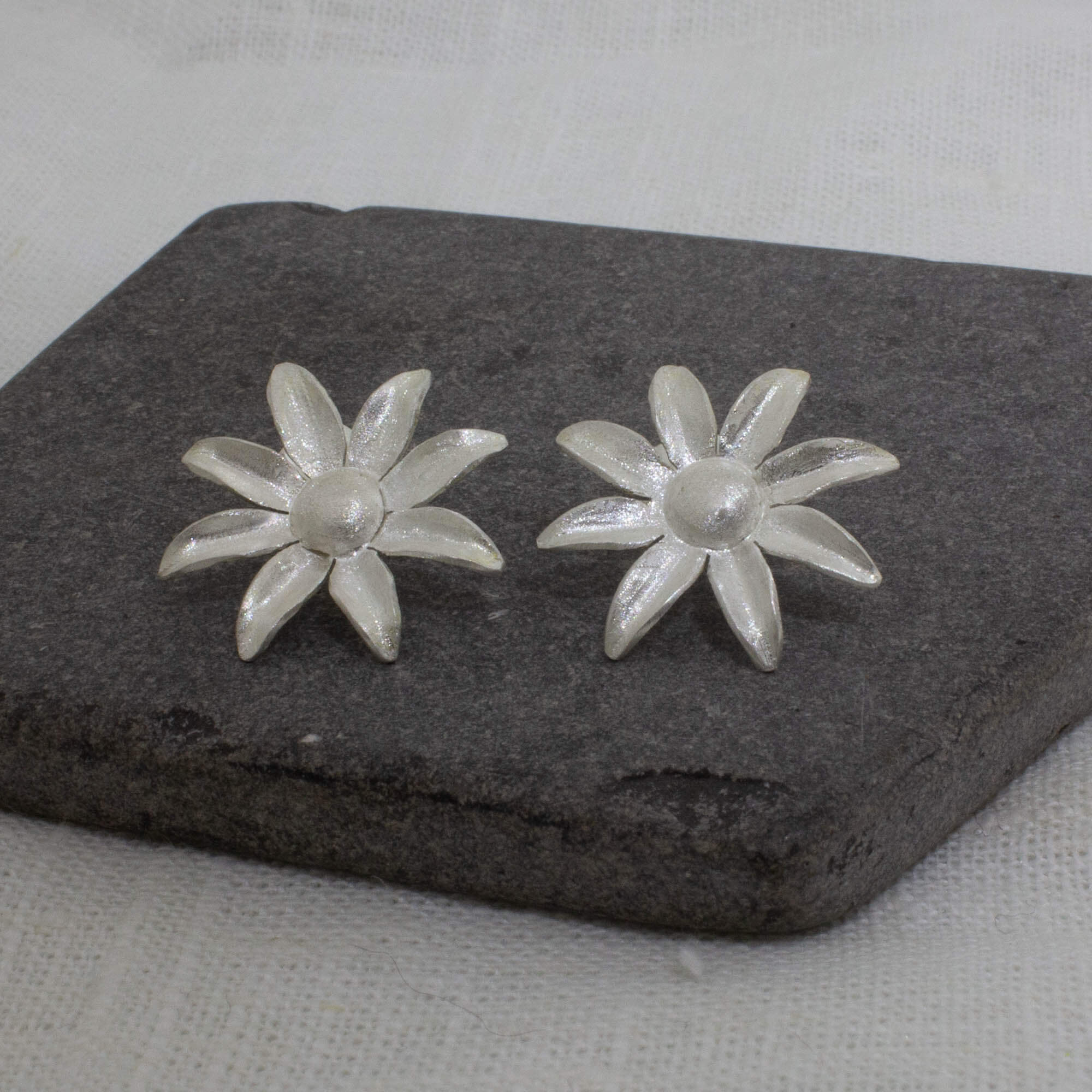 Large brushed sterling silver daisy flower stud earrings displayed on a dark grey slate