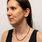 Woman wearing a red garnet beaded necklace and gold earrings against a plain background