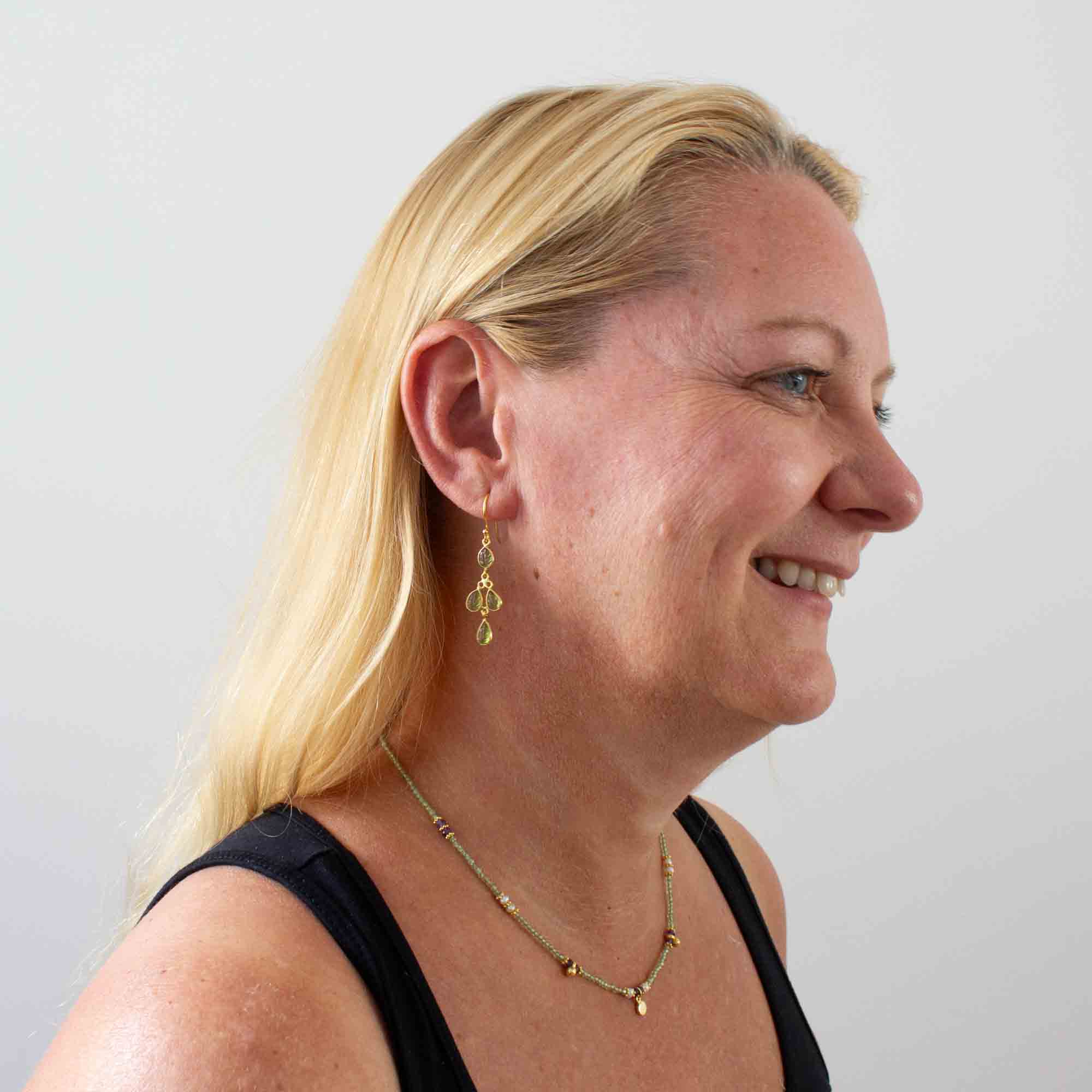 Model wearing Drop earrings featuring 4 small leaf shaped carved peridot gemstones in a simple 18k gold vermeil setting, with a hook fitting