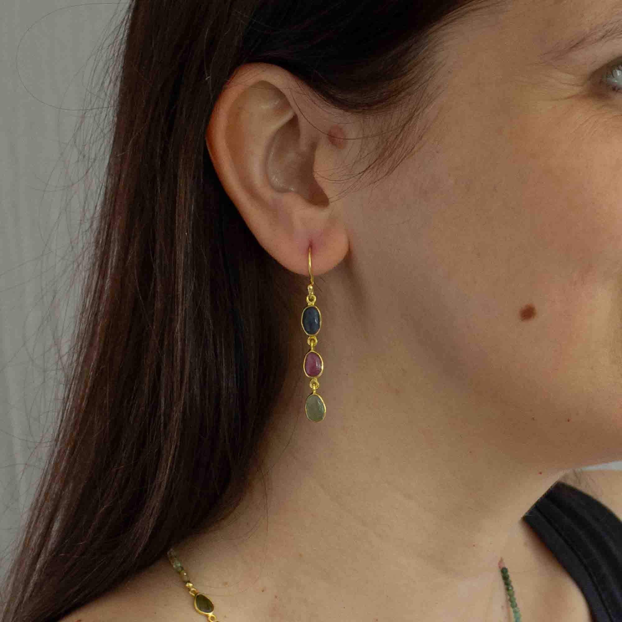 Three stone sapphire drop earrings, featuring oval shaped pink, blue and green sapphire gemstones in a simple gold vermeil setting, with a hook fitting.