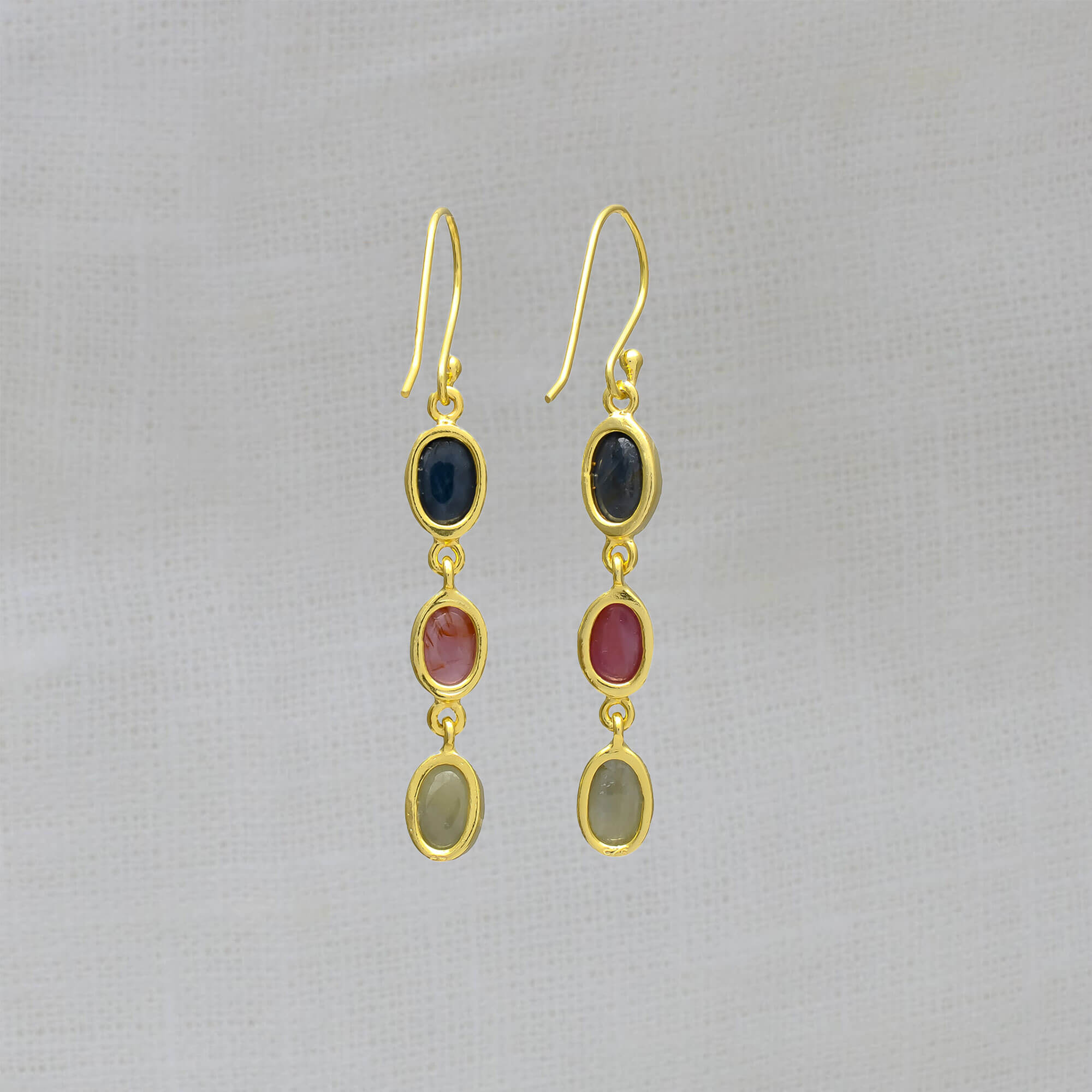 Three stone sapphire drop earrings, featuring oval shaped pink, blue and green sapphire gemstones in a simple gold vermeil setting, with a hook fitting.