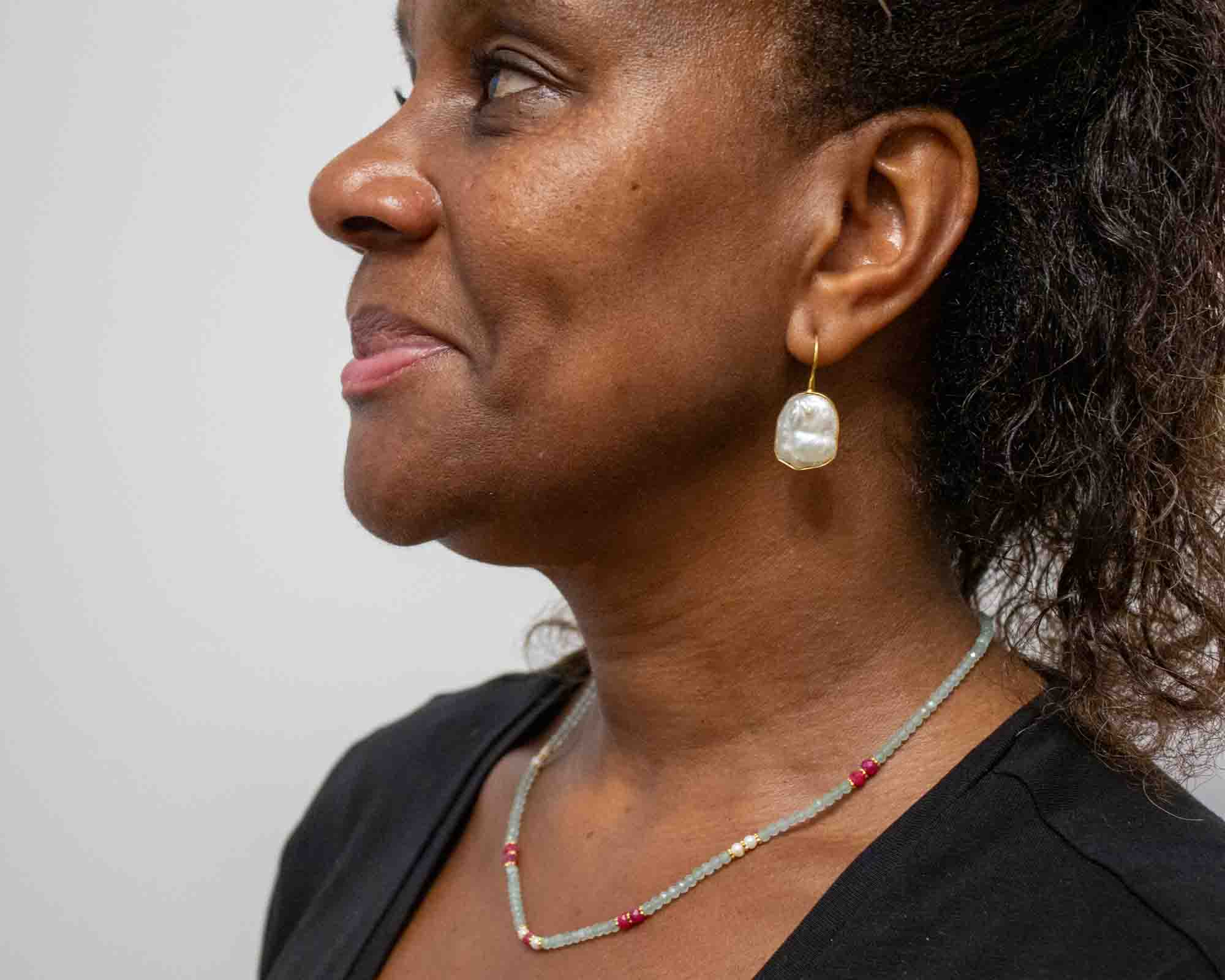 Woman wearing a pearl earring and necklace against a plain background