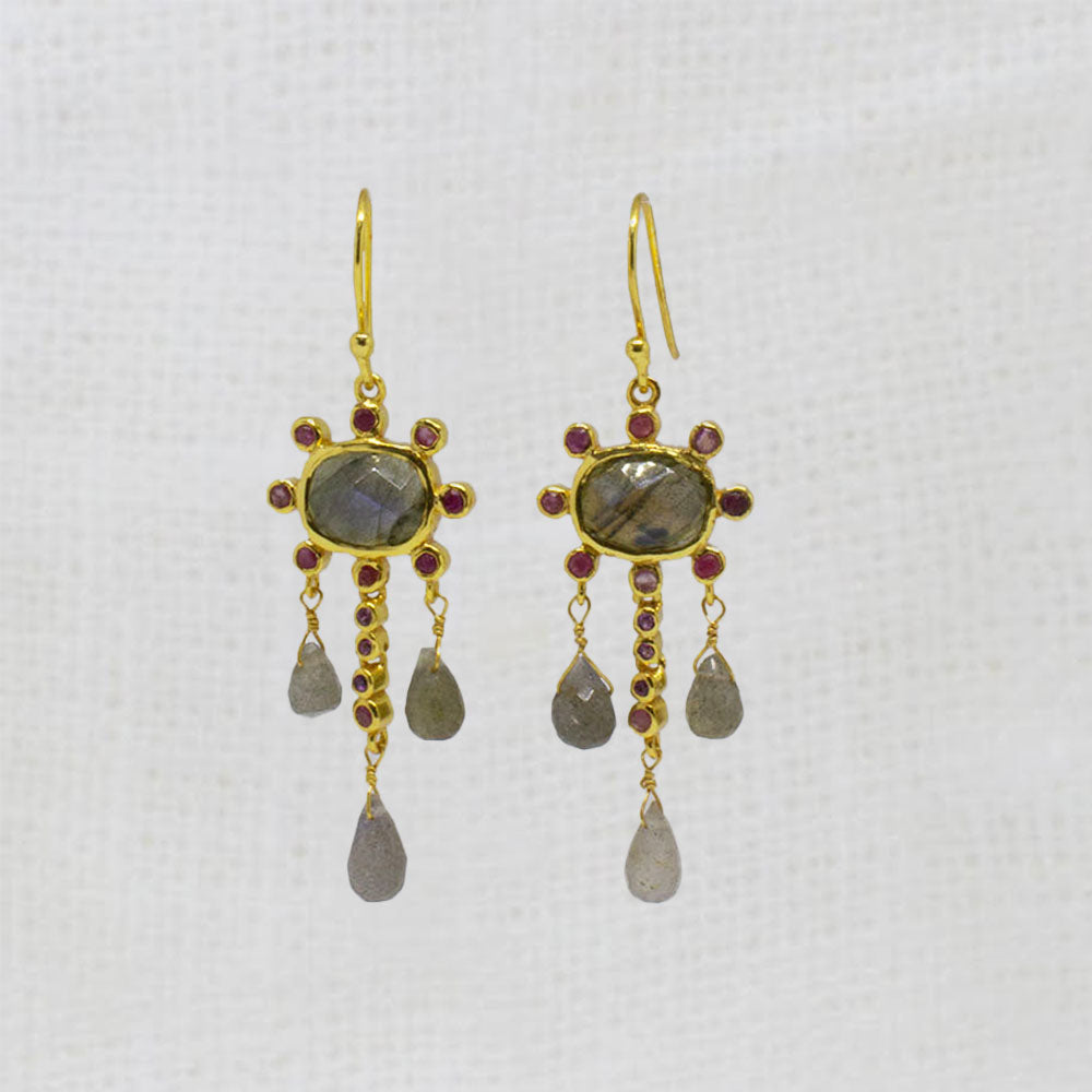 Gold earrings with labradorite and ruby gemstones and dangling beads on a white background