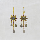 Gold earrings with labradorite and ruby gemstones and dangling beads on a white background