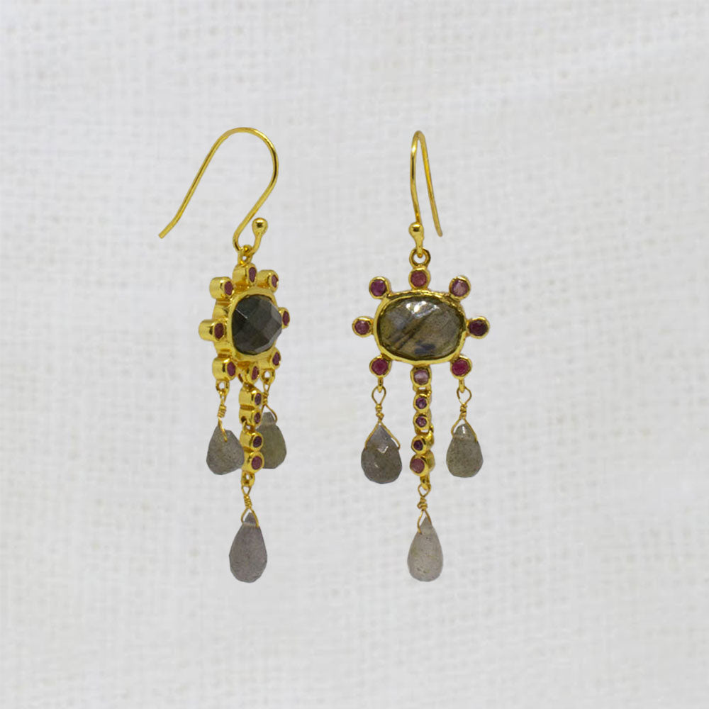 Gold earrings with labradorite and ruby gemstones and dangling beads on a white background