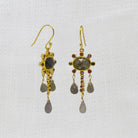 Gold earrings with labradorite and ruby gemstones and dangling beads on a white background