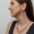 Woman wearing a red garnet gemstone teardrop necklace and matching earrings against a plain background