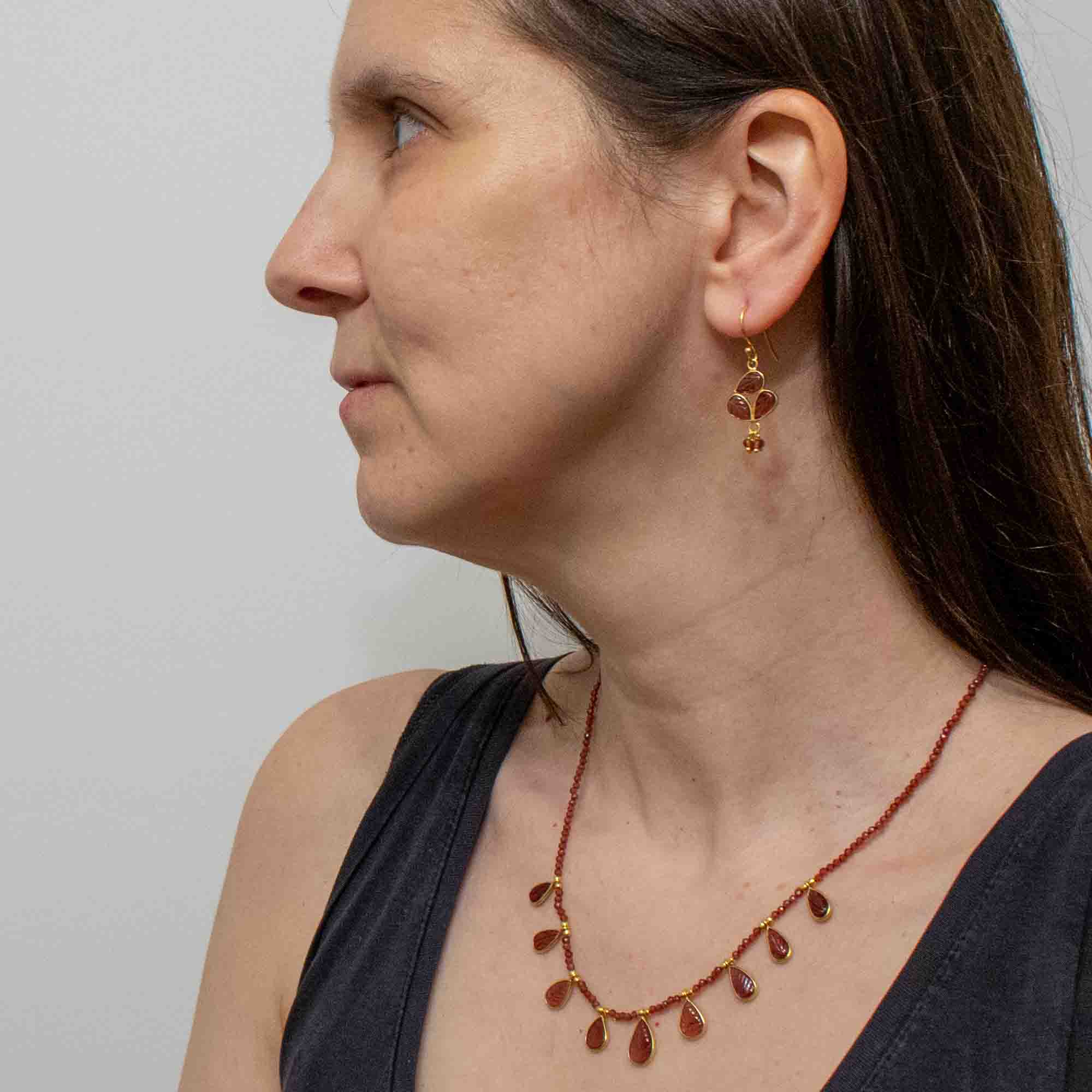 Woman wearing a red garnet gemstone teardrop necklace and matching earrings against a plain background