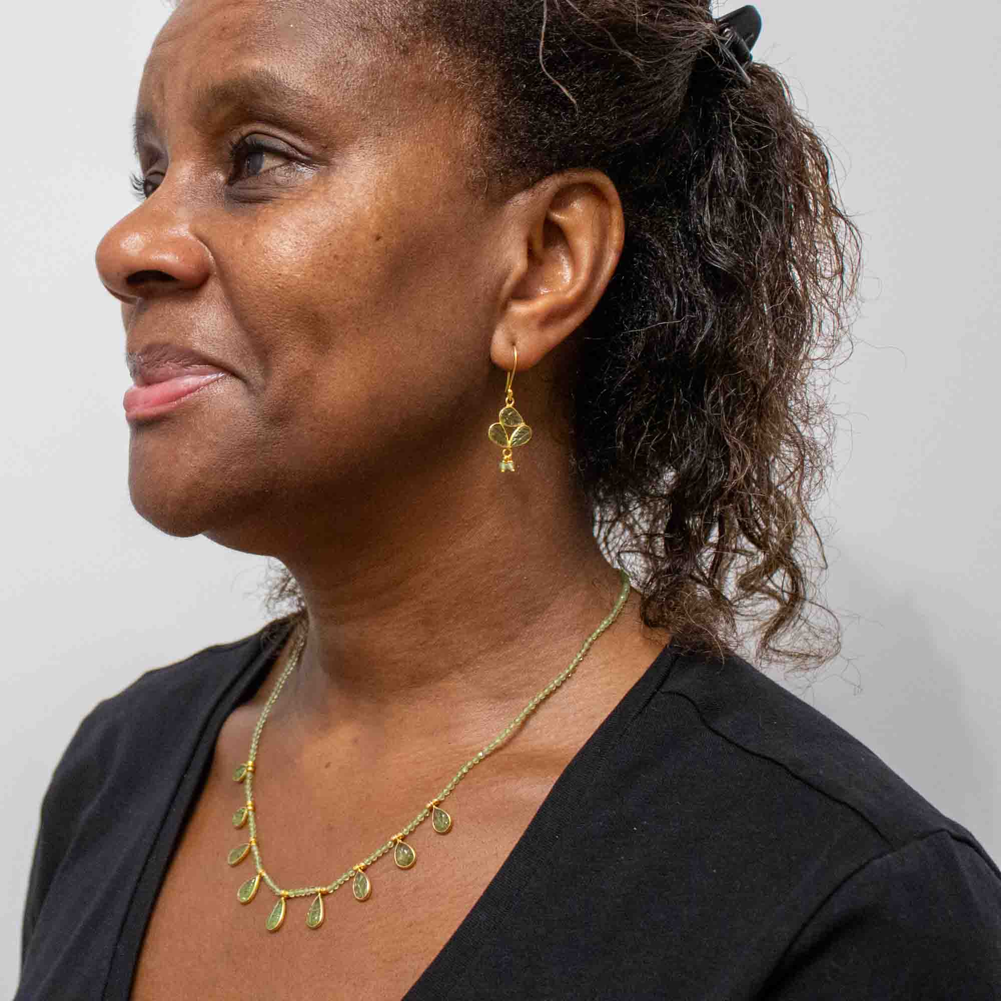 Woman wearing a gold  and peridot necklace and earring against a plain background