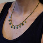 Necklace with green emerald teardrop-shaped beads on a person wearing a black top.