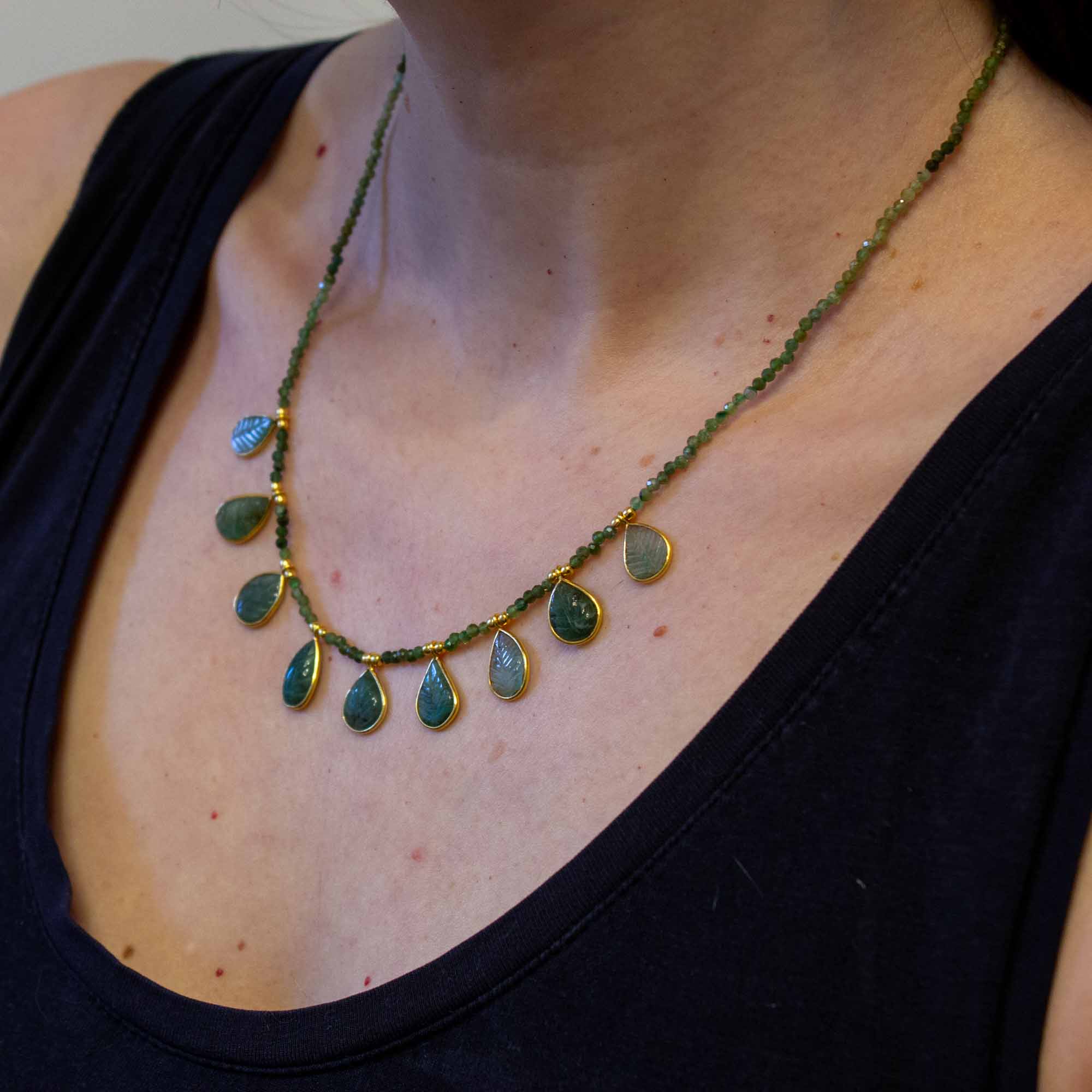 Necklace with green emerald teardrop-shaped beads on a person wearing a black top.