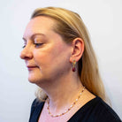 Woman wearing a gold earring with a red gemstone against a plain background