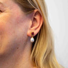 Close-up of an ear wearing a pearl earring with a red gemstone on a white background