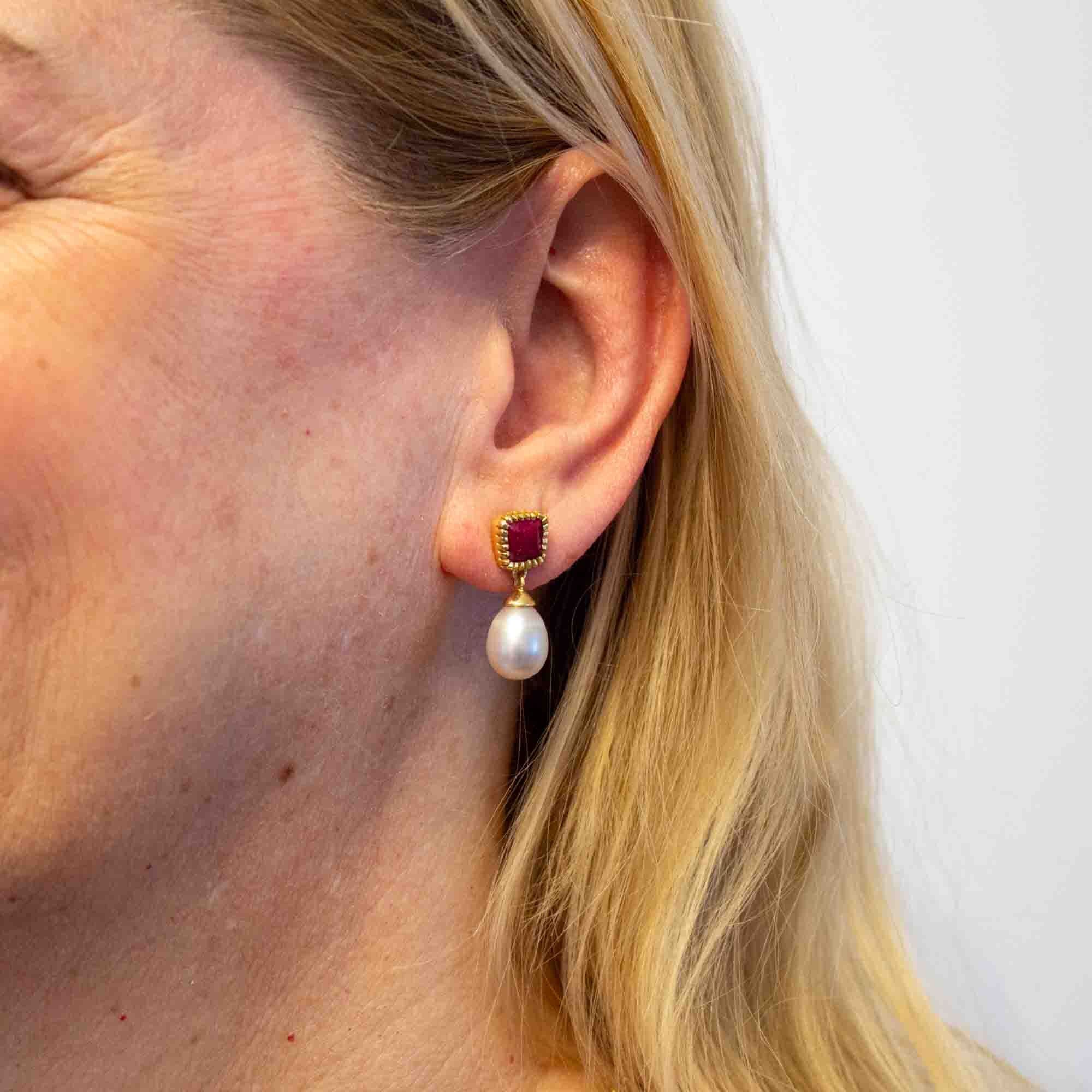 Close-up of an ear wearing a pearl earring with a red gemstone on a white background