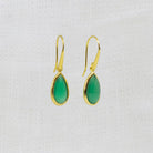 A pair of gold drop earrings with teardrop-shaped green onyx gemstones, displayed on a textured white fabric background.