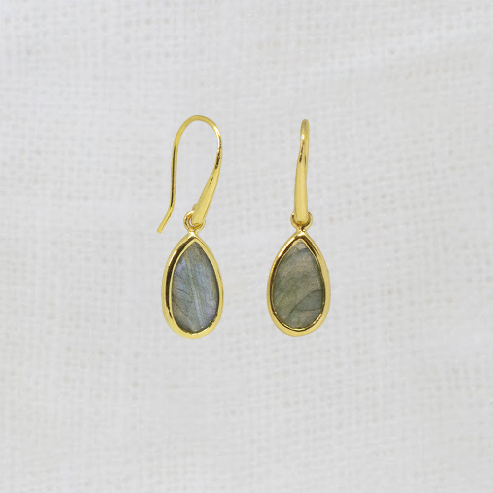 A pair of gold teardrop dangle earrings with gray-green labradorite stones, displayed on a textured white fabric background.