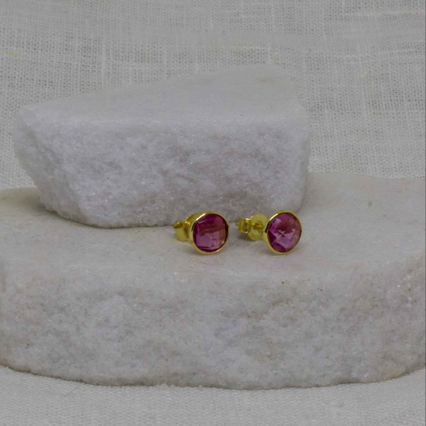 Pair of pink gemstone stud earrings on a textured white surface