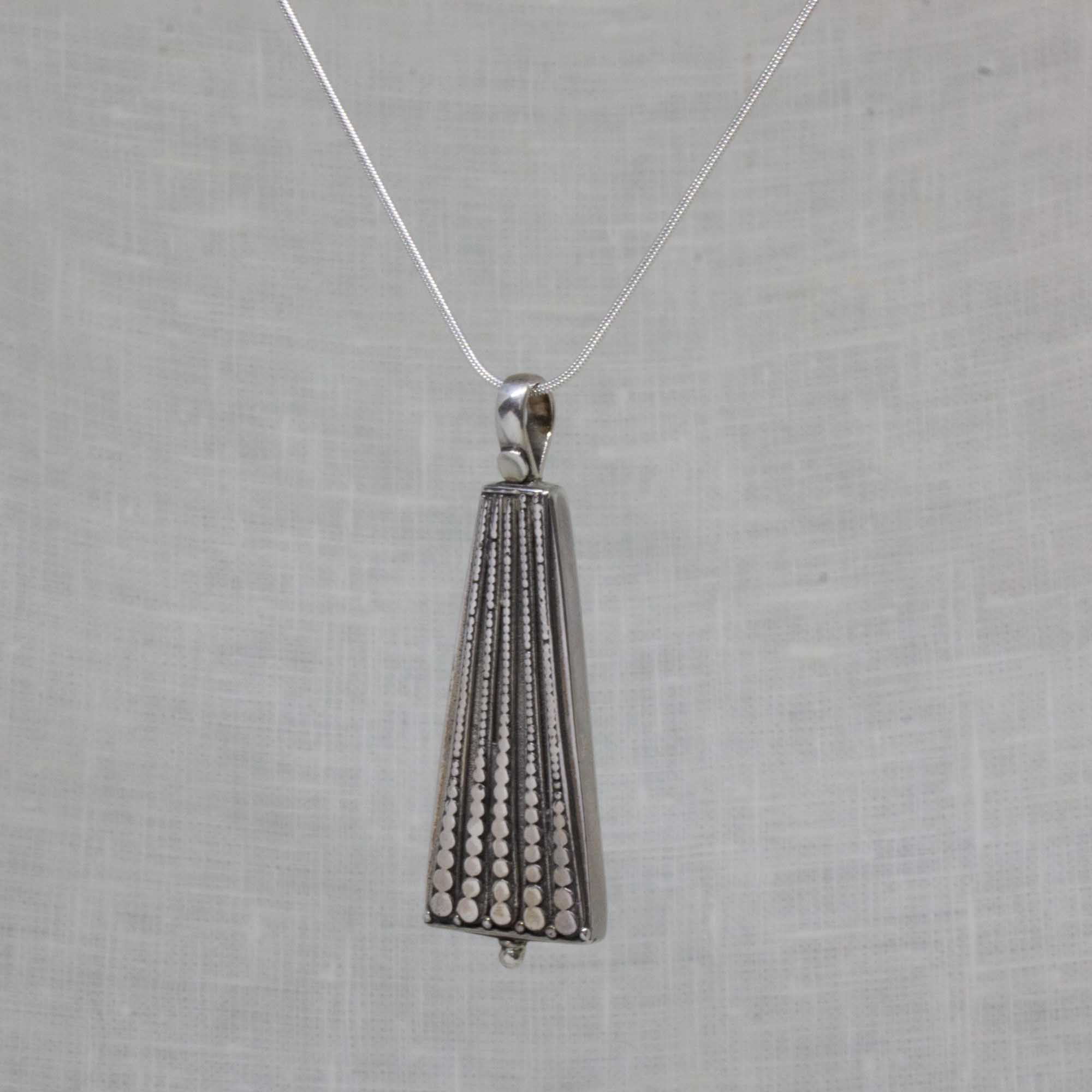 A silver pendant necklace featuring a geometric, cone-shaped design with vertical rows of small clear stones, suspended from a delicate silver chain against a textured light gray background.