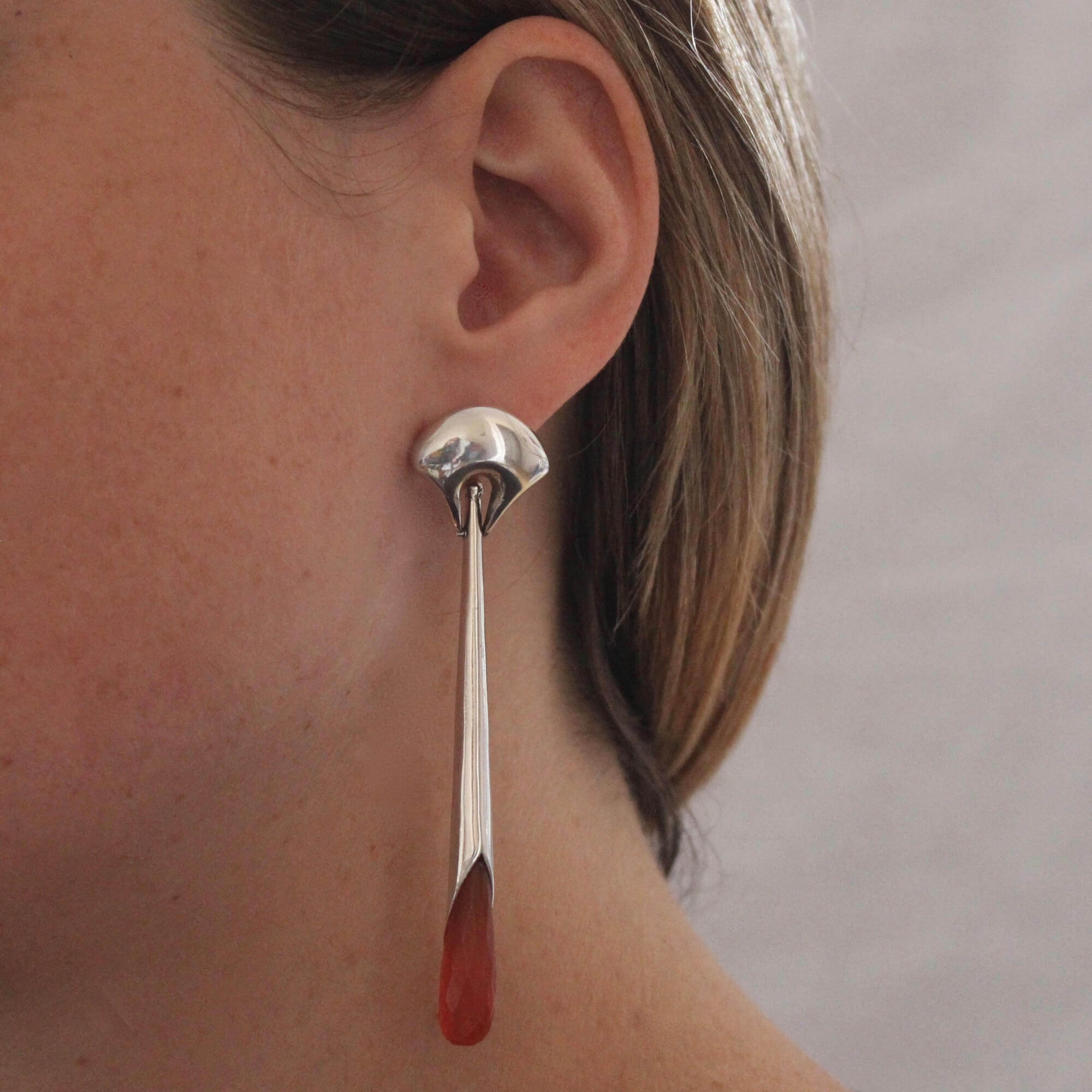 Long statement earrings in sterling silver with a curved stud and long drop with faceted carnelian gemstone